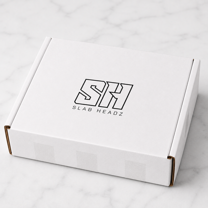 A white cardboard product box with a black outlined 'SH SLAB HEADZ' logo on the lid, photographed on a light marble surface.